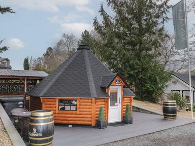 A small wooden cabin with a steep roof and a white door on a deck with barrels and outdoor seating at The Hideaway in Dungiven Londonderry