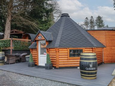 A small wooden cabin with a black shingled roof on a deck with a Guinness barrel and outdoor seating at The Hideaway in Dungiven Londonderry