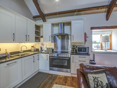 A kitchen with white cabinets a black countertop a stainless steel oven and stove a microwave and a coffee maker at Upper Calffield Barn Camrose near Haverfordwest