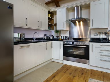 A kitchen with white cabinets stainless steel appliances wooden floor and black countertops at Upper Calffield Barn in Camrose near Haverfordwest