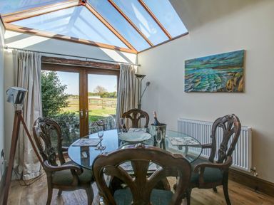 A dining area with a glass table and wooden chairs under a skylight and patio doors at Upper Calffield Barn in Camrose near Haverfordwest