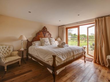 A bedroom with a wooden bed and white linens next to French doors opening to a garden at Upper Calffield Barn in Camrose near Haverfordwest