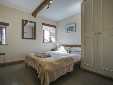 A bedroom with a bed covered with beige blankets two windows a wardrobe and a wall mirror at Upper Calffield Barn Camrose near Haverfordwest