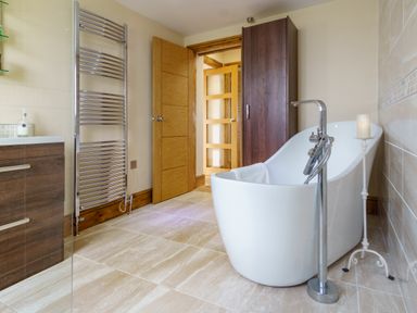 A bathroom with a freestanding bathtub a wooden cabinet a towel radiator and a candle stand at Upper Calffield Barn in Camrose near Haverfordwest