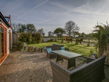 A garden patio with outdoor furniture and a fenced grassy area with horses at Upper Calffield Barn in Camrose near Haverfordwest