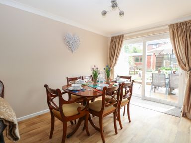 A dining area with wooden table and chairs set for six with wall decoration and sliding glass door to a garden at White Lion Retreat in Cromer