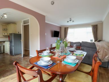 A dining table set with bowls and wine glasses in a room with an archway leading to a kitchen and a sofa near a window at White Lion Retreat in Cromer