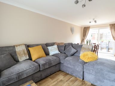 A living room with a gray sectional sofa and cushions next to a dining area with a table and chairs by glass doors at White Lion Retreat in Cromer