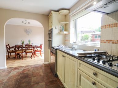 A kitchen with wooden cabinets, a gas stovetop, a sink under a window, and a dining area with a wooden table and chairs in the background at White Lion Retreat in Cromer