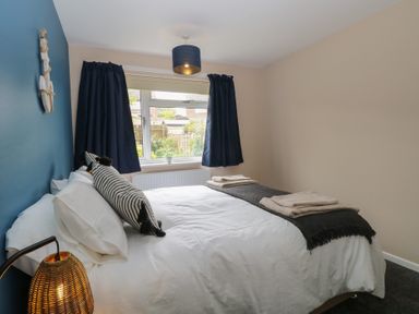 A bedroom with a bed with white bedding and black striped pillows a window with dark curtains and a bedside lamp at White Lion Retreat in Cromer