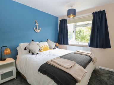 A bedroom with a bed with cushions and folded towels a nightstand with a lamp curtains and a window at White Lion Retreat in Cromer
