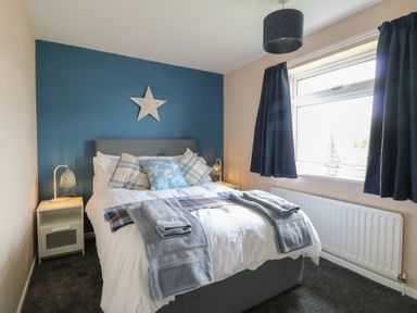 A bedroom with a double bed blue accent wall star decoration bedside tables lamps and a window with blue curtains at White Lion Retreat in Cromer