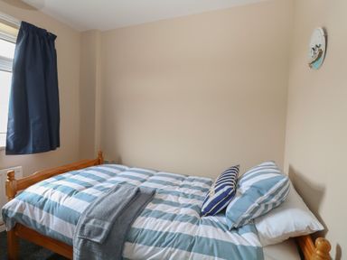 A bedroom with a wooden bed striped bedding and two pillows near a window with dark curtains at White Lion Retreat in Cromer