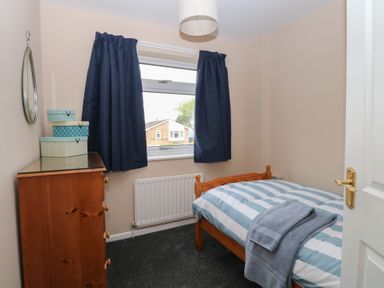 A small bedroom with a wooden bed and chest of drawers with boxes on top at White Lion Retreat in Cromer