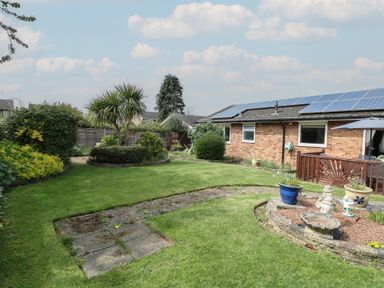 A garden with grass, shrubs, and a small patio next to a brick house with solar panels on the roof at White Lion Retreat in Cromer