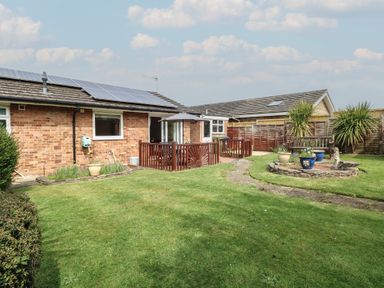A backyard with green lawn, potted plants, wooden deck with umbrella, and a bench near fences at White Lion Retreat in Cromer