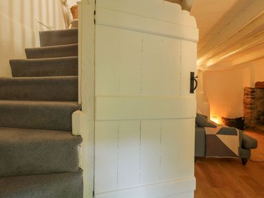 A carpeted staircase next to a white wooden door opening to a room with a sofa and a fireplace at 3 Cumberland Cottages in Ringmore