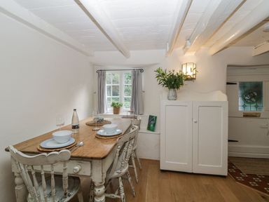 A dining area with a wooden table and chairs near a window and a white cabinet with flowers at 3 Cumberland Cottages Ringmore