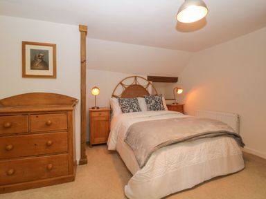 A bedroom with a double bed two bedside tables with lamps a wooden dresser and a framed picture on the wall at 3 Cumberland Cottages in Ringmore