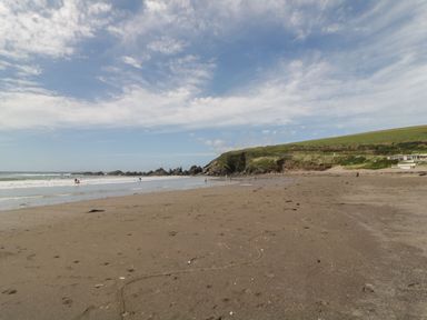 A sandy beach with people near the water and grassy hills in the background at 3 Cumberland Cottages Ringmore