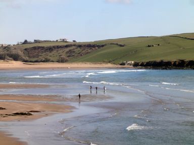 A beach with four people walking in shallow water and green hills in the background at 3 Cumberland Cottages in Ringmore