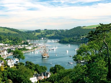 A river with boats and a town along its banks surrounded by green hills and trees at 3 Cumberland Cottages in Ringmore