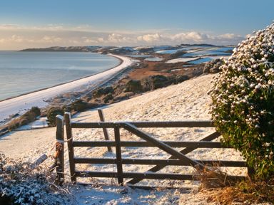 A coastal landscape with snow-covered hillside and a wooden gate overlooking a beach and sea at 3 Cumberland Cottages in Ringmore