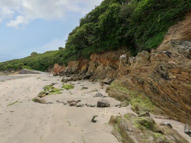 A sandy beach with rocks and green vegetation on a cliffside at 3 Cumberland Cottages in Ringmore
