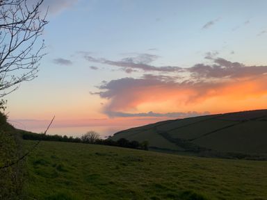 Sunset over green fields and hills with some trees and clouds in the sky at 3 Cumberland Cottages in Ringmore