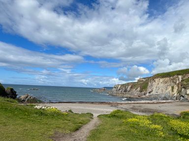 A coastal landscape with a beach grassy area and cliffs under a partly cloudy sky at 3 Cumberland Cottages in Ringmore