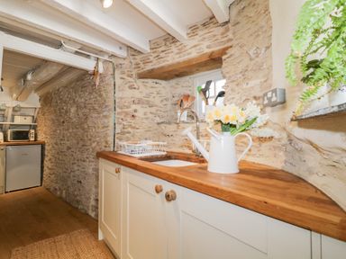A kitchen with wooden countertops white cabinets and stone walls at 3 Cumberland Cottages in Ringmore