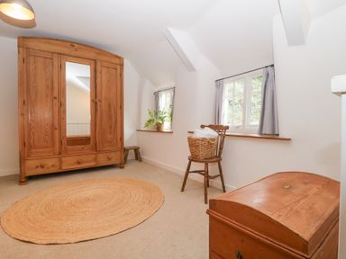 A room with a wooden wardrobe a chair with a basket two windows and a wooden chest at 3 Cumberland Cottages Ringmore