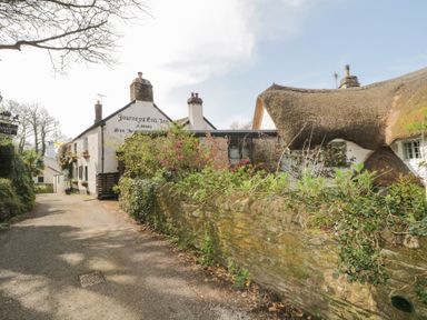 A stone cottage with thatched roof and garden by a gravel road at 3 Cumberland Cottages in Ringmore