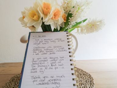 A notebook with handwritten notes and a bouquet of flowers on a wooden table at 3 Cumberland Cottages in Ringmore