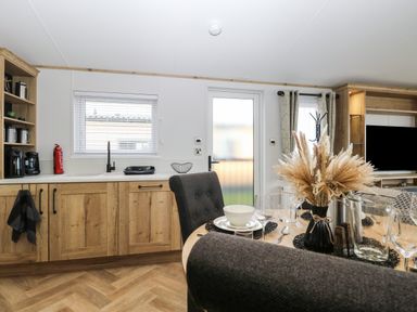 A kitchen and dining area with wooden cabinets and a table with place settings and dried plants at Dorchester in Broomholm near Mundesley