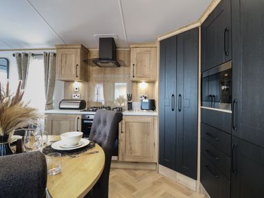 A kitchen with wooden and black cabinets a dining table with place settings and grey chairs at Dorchester in Broomholm near Mundesley
