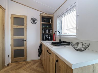 A kitchen with wooden cabinets a sink a window with blinds and kitchen appliances at Dorchester in Broomholm near Mundesley