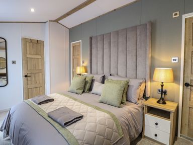 A bedroom with a bed bedside tables lamps and wooden doors at Dorchester in Broomholm near Mundesley