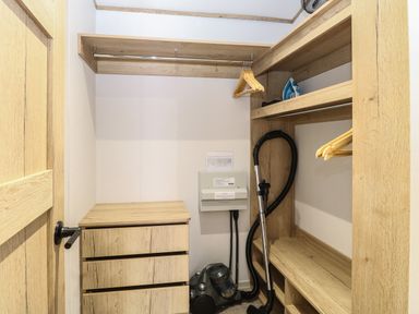 A small closet with wooden shelves a vacuum cleaner an iron and wooden hangers at Dorchester in Broomholm near Mundesley