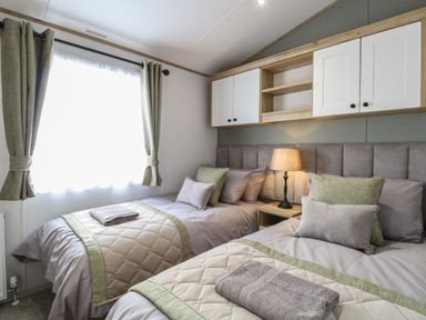 A bedroom with two single beds lamps and storage cabinets at Dorchester in Broomholm near Mundesley