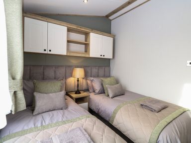 A bedroom with two single beds a lamp on a nightstand and wall cabinets above the beds at Dorchester in Broomholm near Mundesley
