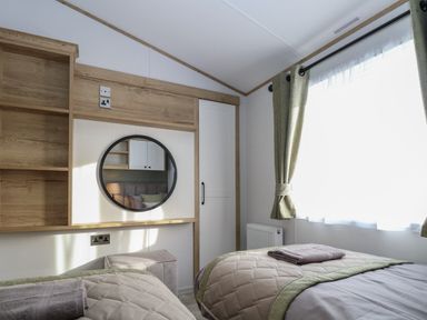 A bedroom with two single beds a round mirror and a window with curtains at Dorchester in Broomholm near Mundesley