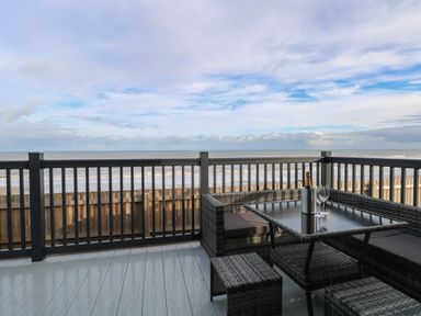 A patio with rattan furniture and a bottle of champagne with glasses overlooking the ocean at Dorchester in Broomholm near Mundesley