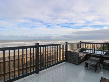 A balcony with wicker seating and a table overlooking a beach and ocean at Dorchester in Broomholm near Mundesley
