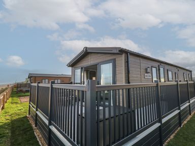 A fenced outdoor deck area attached to a modern modular home under a partly cloudy sky at Dorchester in Broomholm near Mundesley