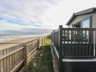 A view of a fenced walkway between a beach and a cabin with a porch at Dorchester in Broomholm near Mundesley