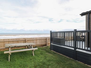 A wooden picnic table on grass near a fenced deck overlooking the ocean at Dorchester in Broomholm near Mundesley