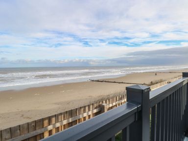 A sandy beach with waves and wooden fences viewed from a balcony at Dorchester in Broomholm near Mundesley