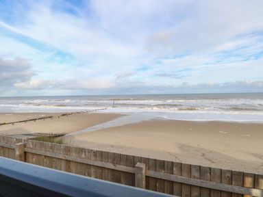 A sandy beach with waves and a wooden fence in the foreground at Dorchester in Broomholm near Mundesley