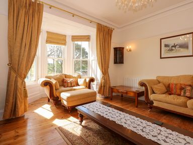A living room with beige sofas a large window with curtains and a wooden coffee table at Fir Grove in Menai Bridge
